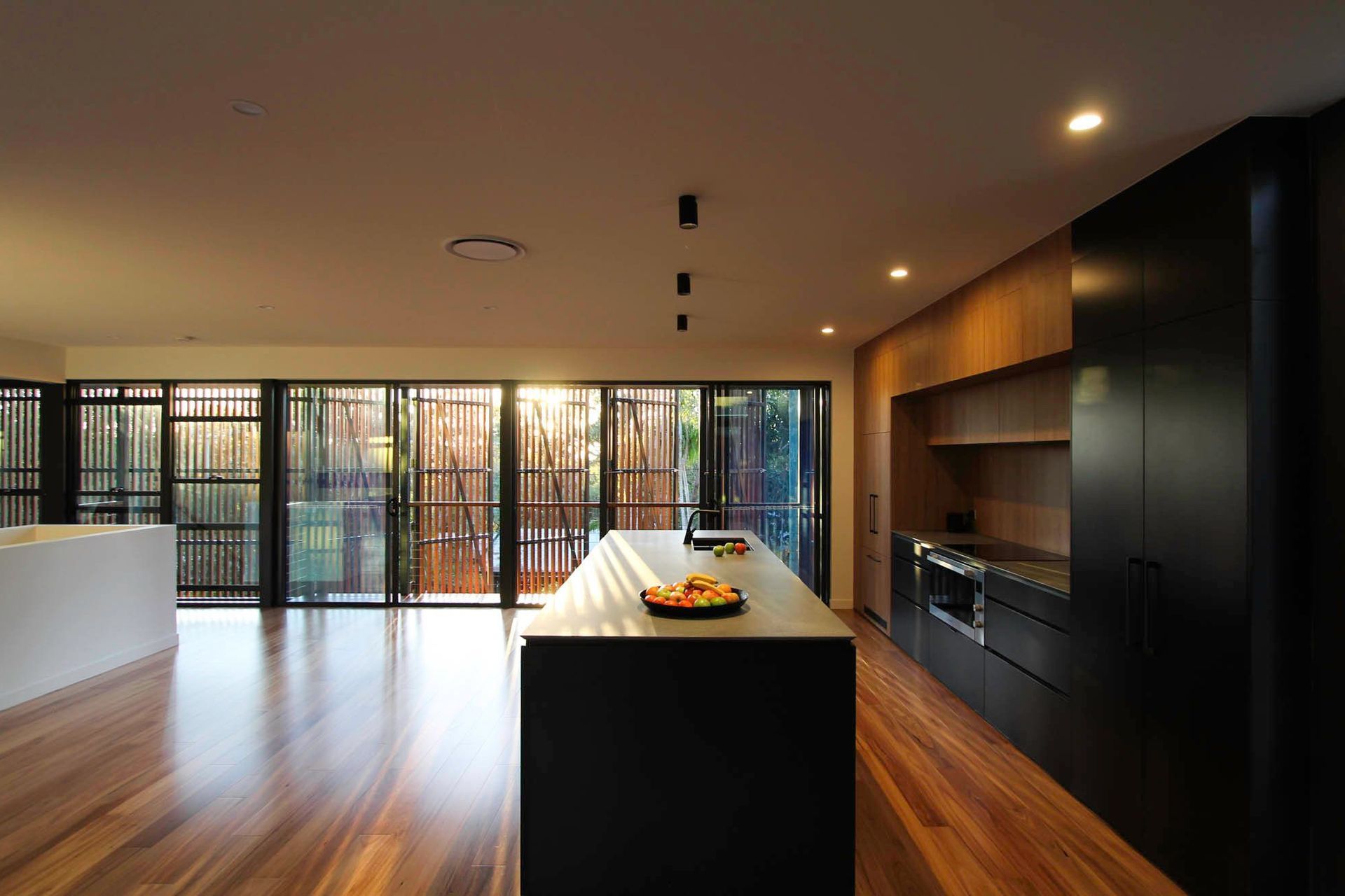 Glennon Residence - Kitchen. Dark island bench framed by full height glazing.