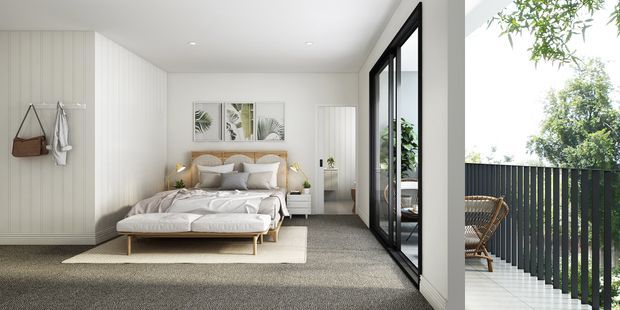 Bright contemporary bedroom with a low upholstered bed, soft neutral bedding, pale vertical wall panelling, carpeted flooring, minimalist bedside tables and framed botanical artwork. Full-height black-framed glazing opens visually onto a narrow balcony or terrace with outdoor seating and garden views.