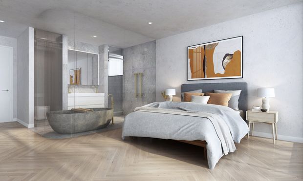 Contemporary bedroom suite with a freestanding stone bathtub positioned beside the bed, a glass-enclosed shower area, pale textured walls, light herringbone timber flooring, and a muted upholstered bed with neutral bedding. Abstract artwork and minimalist bedside furniture add warm tonal accents.