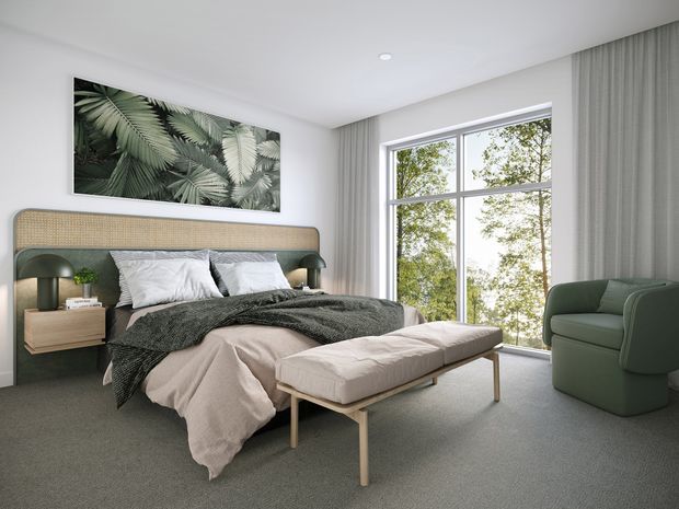 A serene contemporary bedroom with a large upholstered bed featuring a woven cane-style headboard, dark green integrated bedside surfaces and lamps, neutral bedding, and a matching upholstered bench. Floor-to-ceiling curtains frame a large divided window, while a green armchair and botanical wall artwork add natural accents. The room has carpeted flooring, white walls, and a clean, softly lit design.