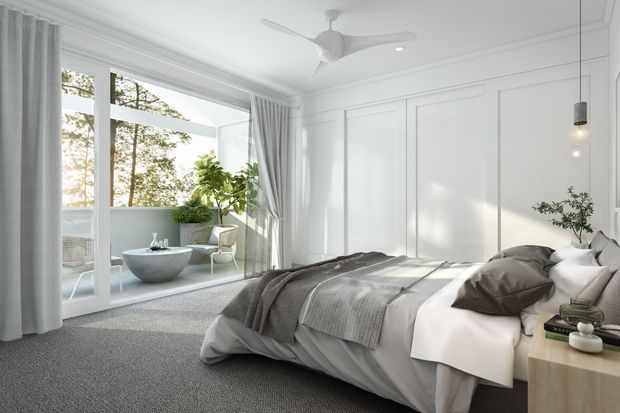 Bright, refined bedroom with white decorative wall panelling, soft grey carpet, layered neutral bedding, a timber bedside table, pendant lighting, and full-height glazing opening to a furnished balcony or sunroom. Indoor plants and views of trees add a natural connection to the outdoors.