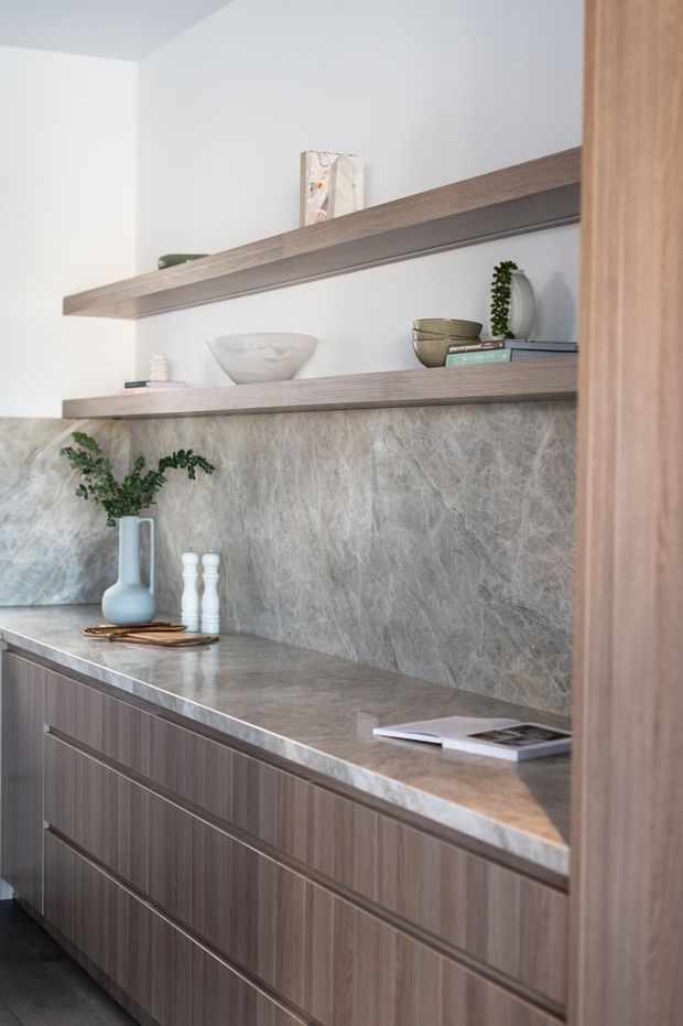 A refined built-in cabinetry and display shelving installation, featuring dark wood-grain drawers, a grey natural-stone benchtop and matching stone splashback, with open timber shelves styled with restrained decorative objects and greenery.