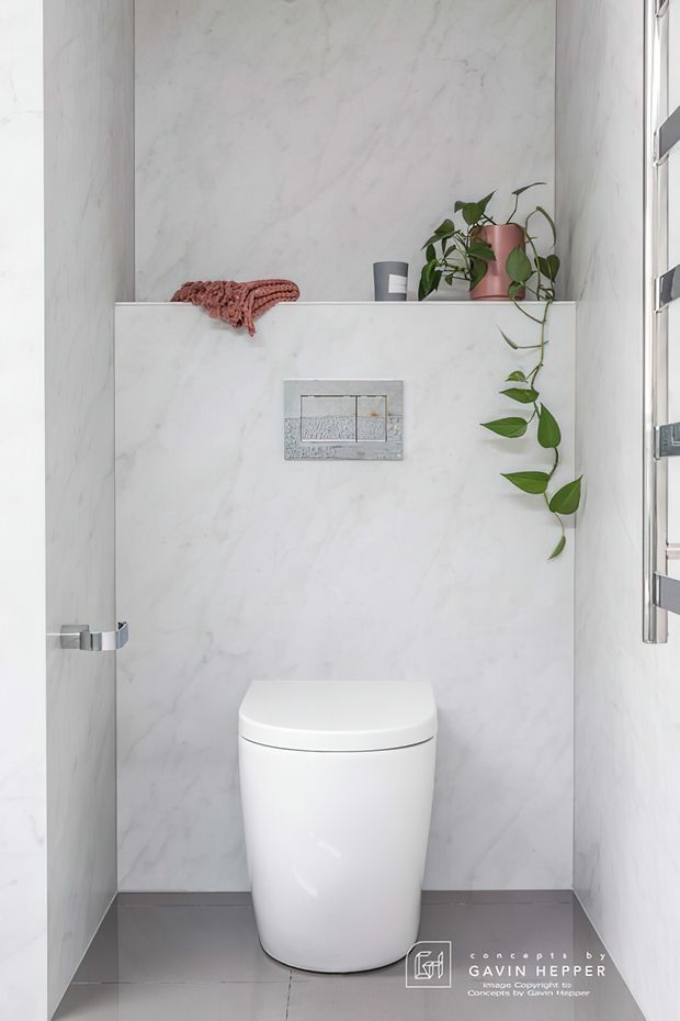 Compact contemporary bathroom or powder room featuring a wall-hung toilet, dual-flush plate, full-height pale marble-look wall surfaces, grey floor tiles, chrome fittings, a recessed shelf, and a trailing potted plant. The space is bright, clean, and minimalist.