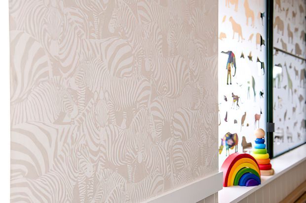 A bright children's room corner featuring a pale animal-patterned wallpapered wall, white trim and sill, and a deep window recess displaying colourful animal decals and a rainbow stacking toy. The space has a playful, light, contemporary feel.