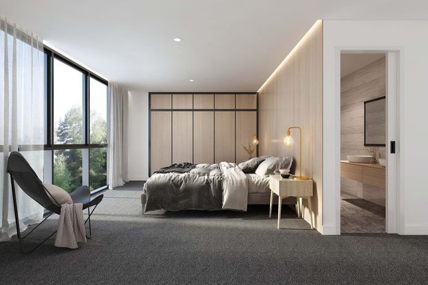 A contemporary bedroom with floor-to-ceiling corner glazing, sheer curtains, a low upholstered bed, dark grey carpet, and warm timber-toned built-in wall panelling. A slim bedside table and warm pendant lamp sit beside the bed, while an open doorway reveals a connected bathroom with timber-look wall finishes and a floating vanity.
