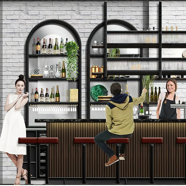 A stylized commercial bar interior with a long dark counter, ribbed vertical-front cabinetry, red upholstered stools, extensive open shelving, and an arched recessed display niche. The shelves hold bottles, glasses, barware, and decorative objects, with black metal framing against a white-painted brick wall. Two bartenders and a seated customer are shown, suggesting a restaurant or hospitality setting.