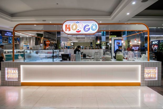 A bright mall food-court kiosk storefront featuring a playful “HOOGO” illuminated sign, orange-trimmed glass display counters, ribbed illuminated front cladding, and tiled flooring. Other food outlets and mall circulation areas are visible in the background.