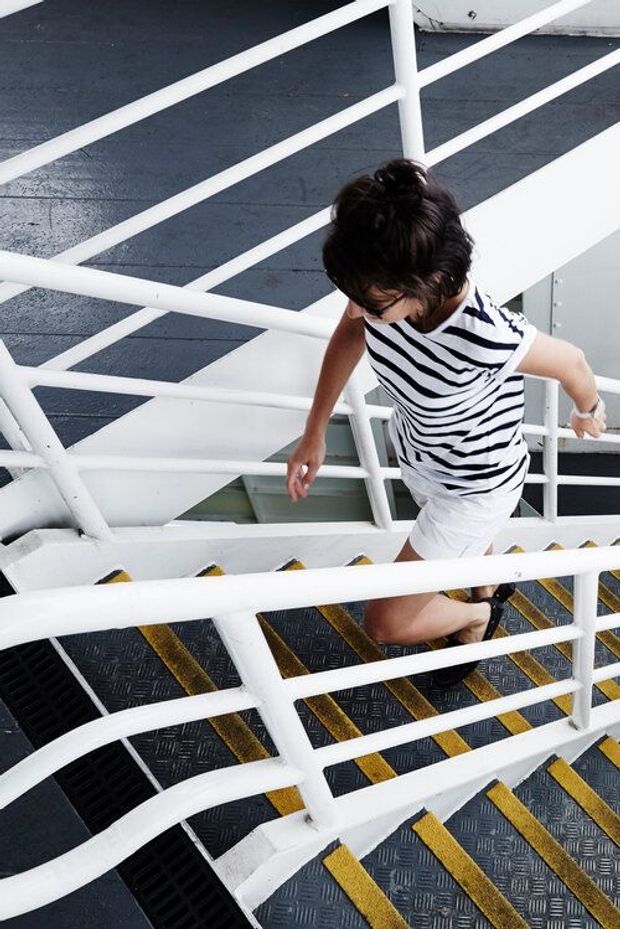 A person ascending an industrial-looking stairway with white metal handrails, dark textured treads, and contrasting yellow safety-edge markings. The image focuses on the staircase and its structural railings rather than a residential room.