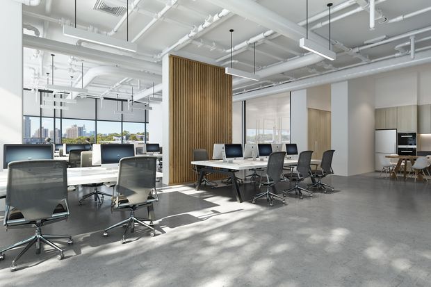 Bright contemporary open-plan office with rows of workstations, meeting tables, ergonomic task chairs, floor-to-ceiling windows, and a compact kitchenette at the rear. The space has exposed white services and ductwork, suspended linear lighting, polished concrete flooring, and a vertical timber slat feature wall. A cityscape is visible through the glazing.