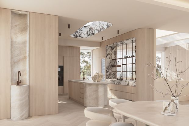 A refined open-plan kitchen and dining area in a warm neutral palette. Pale timber-look cabinetry forms a wall of integrated storage, while a curved stone kitchen island sits centrally beneath a sculptural marble-patterned pendant light. A large marble-look splashback or feature wall with dark framed glazing adds contrast, and a rounded dining table with upholstered chairs occupies the foreground. Natural light enters through large windows and a rooflight, creating a bright, softly luxurious interior.