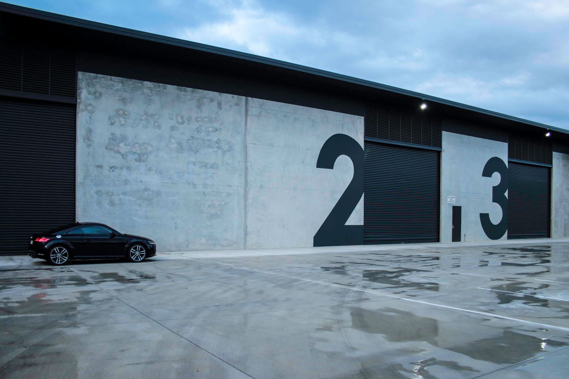 Eniquest Warehouse - Exterior. Tenancy doors marked with bold numbers along the concrete facade.