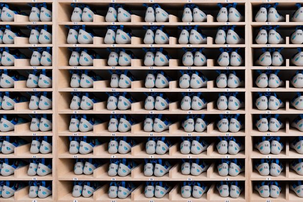 A tightly framed, repetitive storage wall filled with rows of identical white and blue athletic shoes arranged in individual light timber cubbies. The image emphasizes organized retail or product-display shelving rather than a conventional residential room.