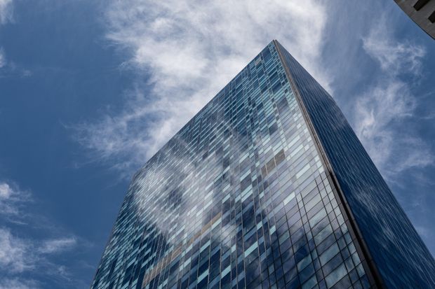 Low-angle exterior view of a tall contemporary high-rise tower with extensive blue-tinted glass curtain-wall façades, sharply converging vertical lines, and a pointed corner against a partly cloudy sky.