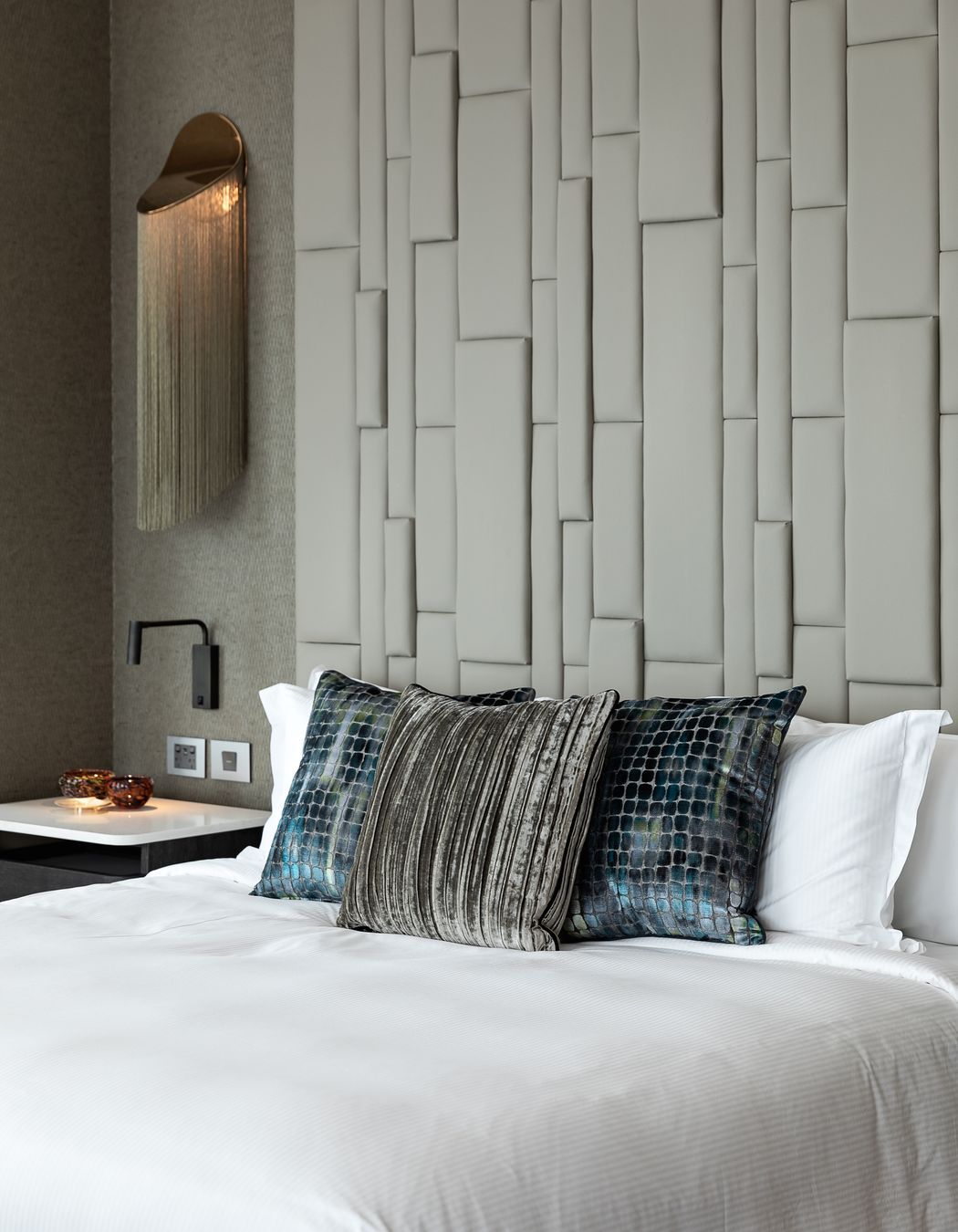 A textured padded headboard makes a grand statement alongside the incredible wall lamp.