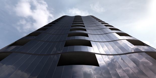 Low-angle exterior view looking up the curved facade of a tall contemporary high-rise building. The dark reflective envelope is composed of vertical panels and repeated recessed or projecting balcony openings, with bright sky reflections across the glazing.