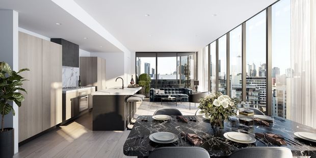 A bright, open-plan high-rise apartment interior combining a contemporary kitchen, dining area, and living space. The kitchen has tall light-wood cabinetry, a dark island with a pale stone or marble benchtop, integrated appliances, and a dark stone splashback. A black marble dining table occupies the foreground, while floor-to-ceiling glazing reveals a dense urban skyline. The space is refined and spacious with a neutral palette, abundant daylight, and high-rise city views.