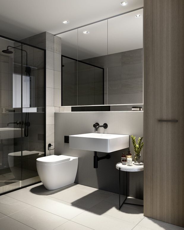 A contemporary bathroom with a frameless black-framed glass shower enclosure, wall-mounted white basin, floating toilet, large mirrored vanity wall, and grey tiled surfaces. A dark textured feature wall behind the basin contrasts with pale floor and wall tiles. Recessed ceiling lights and black tapware create a clean, refined, modern look.