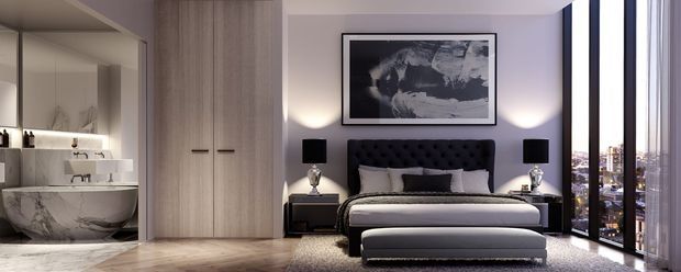 A refined contemporary bedroom with a black tufted upholstered bed, matching bedside tables and lamps, a long upholstered bench, and a large monochrome artwork above the bed. Full-height glazing on the right provides city views, while a partially visible ensuite or dressing area with a sculptural marble-patterned basin appears on the left. The room uses pale timber flooring, dark accents, soft grey textiles, and integrated floor-to-ceiling cabinetry.