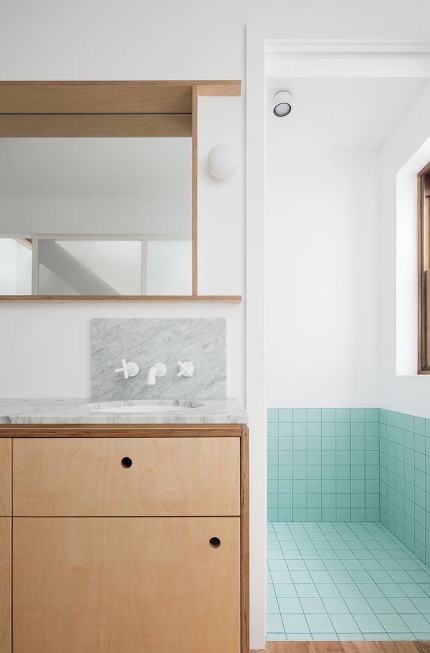 Bright, compact bathroom with a timber vanity featuring flat-front drawers, a pale marble benchtop and backsplash, and an open timber-framed mirror cabinet above. The adjacent shower area is lined with small turquoise square tiles across the walls and floor. White walls, recessed lighting, and a timber-framed window create a clean contemporary look.