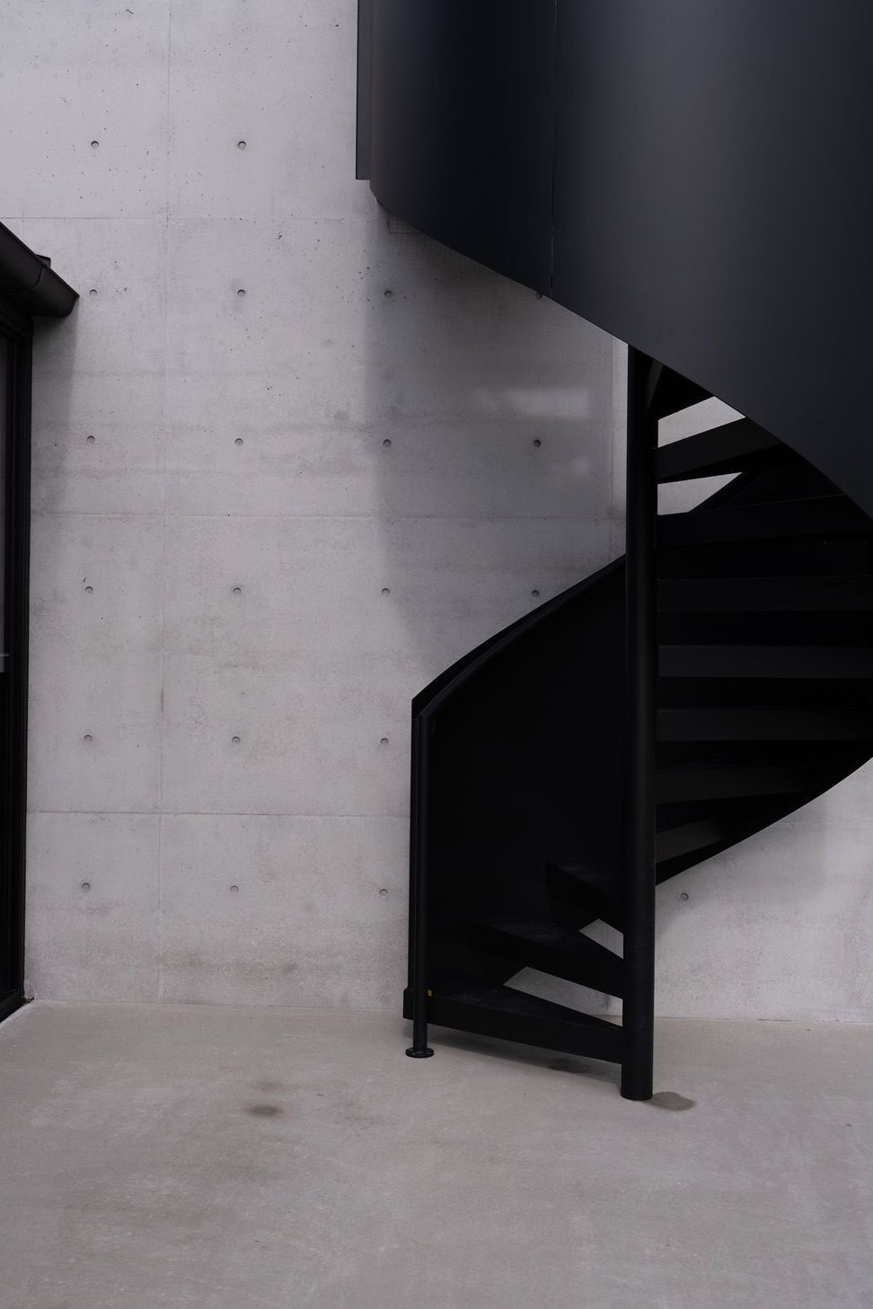 The Farm - Staircase. Black spiral stair against an off-form concrete wall.