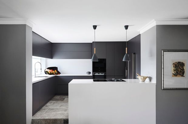 Contemporary L-shaped kitchen with dark matte cabinetry, a bright white island and benchtops, integrated appliances, pendant lighting, and grey tiled flooring. White ceiling cornices and grey walls add a restrained, refined finish.