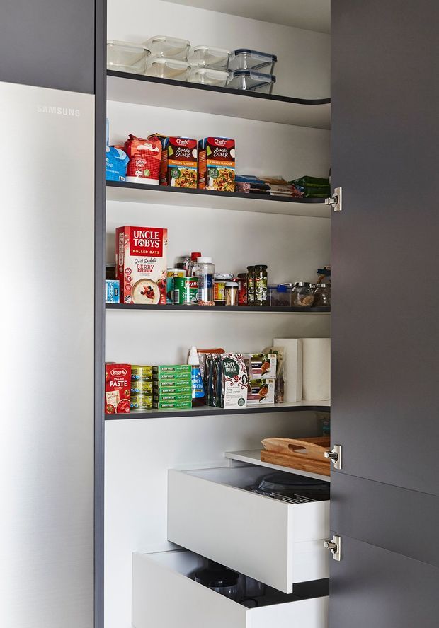 Open tall pantry cabinetry with dark grey doors, white interior shelving, clear storage containers, packaged dry goods, jars, and deep pull-out drawers. The organized food-storage joinery is the dominant subject.