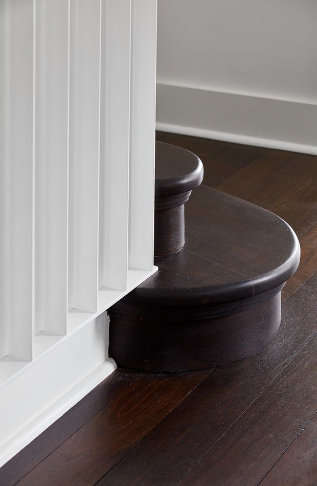 Close-up architectural detail of a curved dark timber staircase with rounded stair treads and a substantial central newel or structural support. White vertical wall panelling and trim frame the stair, contrasting with the dark polished timber flooring and staircase. The image focuses on craftsmanship, joinery, and material contrast rather than a full room view.