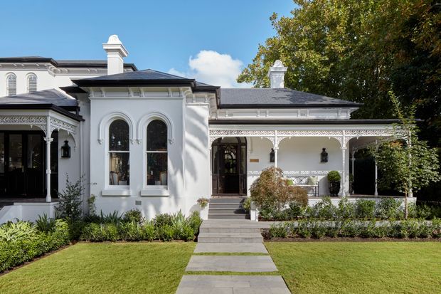 Front exterior view of an elegant white heritage-style residence with ornate arched windows, decorative fretwork, covered verandas, classical chimney detailing, dark hipped roofing, and a landscaped front garden with a paved path leading to the entrance.