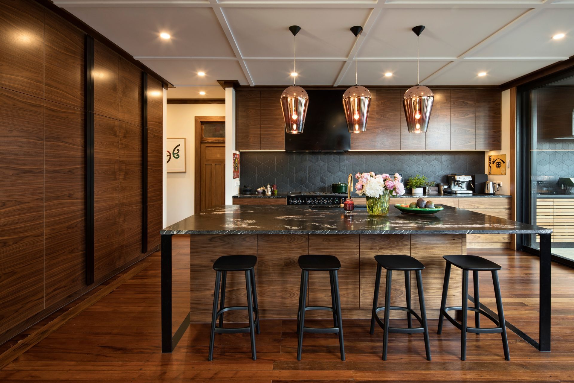 Natural timber finishes and refined detailing define the contemporary kitchen. Walnut cabinetry, a titanium gold granite island and a hidden scullery combine functionality with understated luxury, while large openings connect the space to the outdoor entertaining area.