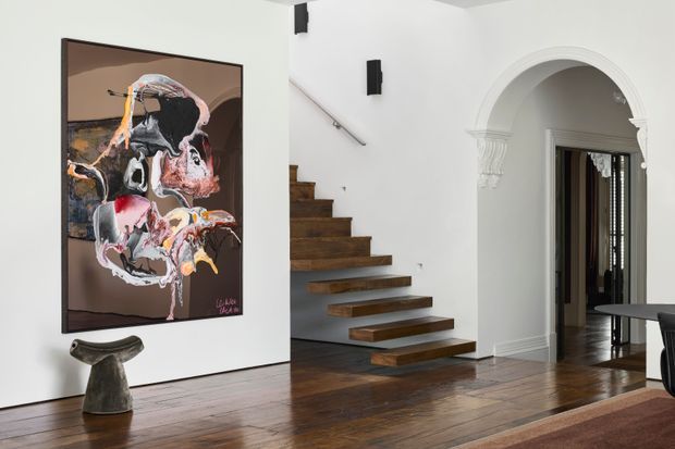 A refined interior hallway and stairway with dark timber flooring and floating timber stairs against white walls. A large abstract artwork and sculptural pedestal accent the space, while an ornate arched opening with classical moulding leads to another room. Black wall-mounted light fixtures and a dark dining table are partially visible.