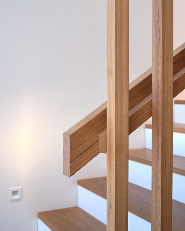 Close-up architectural photograph of a contemporary timber staircase. Warm natural wood treads, stringer, and vertical balusters contrast with white walls and open risers, creating a clean, light-filled stairway detail.