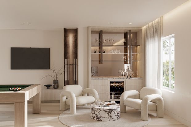 A refined contemporary living room with a built-in bar and display cabinet at the rear, a wall-mounted television, billiards or games table at left, and two rounded cream lounge chairs around a marble coffee table. The room has light timber flooring, neutral walls, recessed ceiling lights, sheer curtains, and a bright window. The styling is softly luxurious with curved furniture and warm integrated lighting.