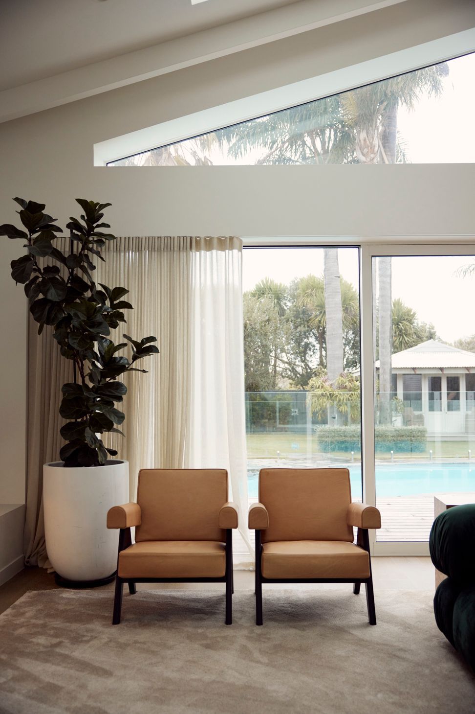 Pierre Jeanneret armchairs framed by stacking slider doors opening to the pool — the rear addition at Point Chevalier Bungalow, where the boundary between inside and out dissolves entirely. In collaboration with Hannah Warren Interiors.