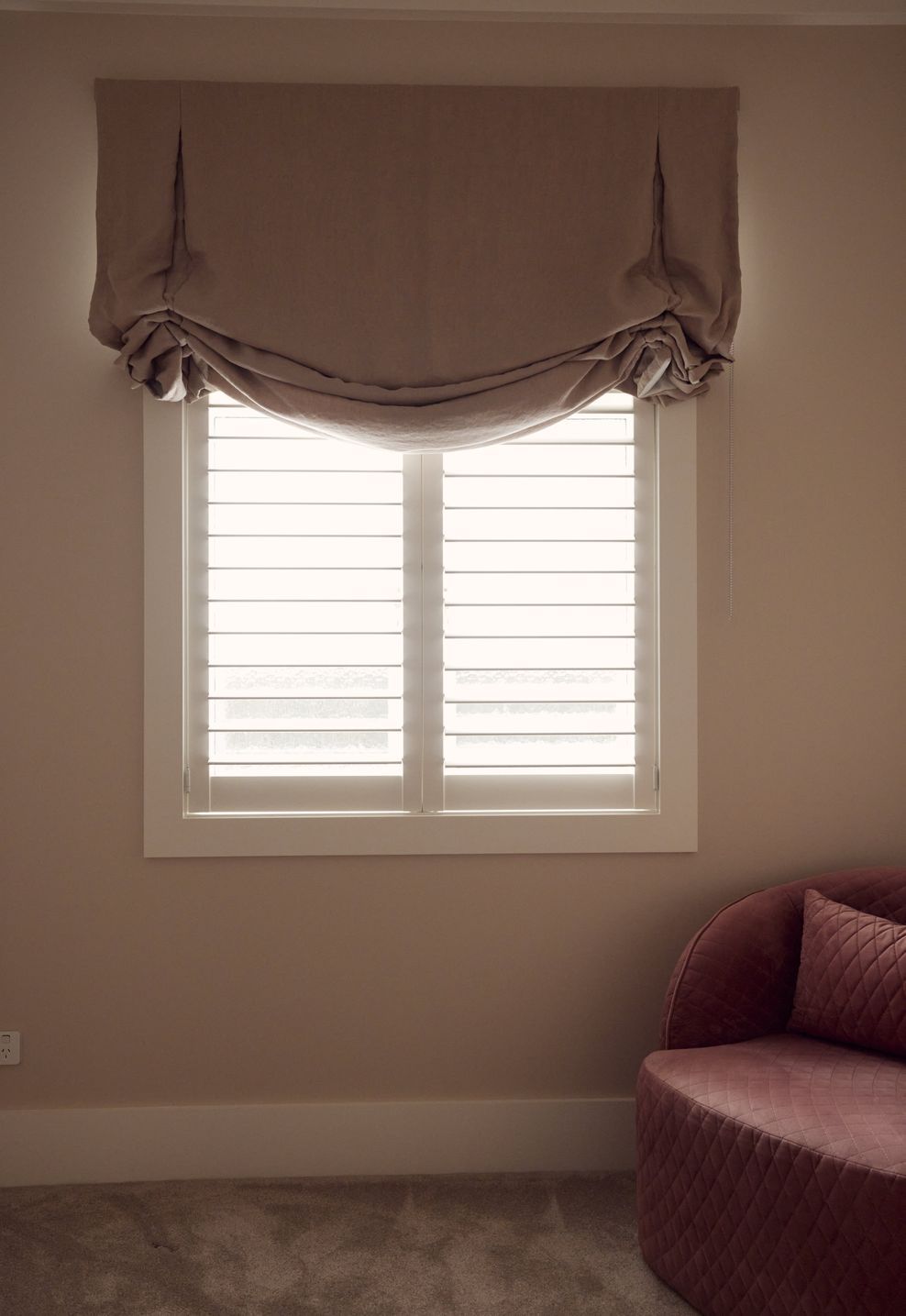 Linen roman blind, plantation shutters and a dusty pink curved sofa — a considered corner of the children's bedroom at Point Chevalier Bungalow. In collaboration with Hannah Warren Interiors.