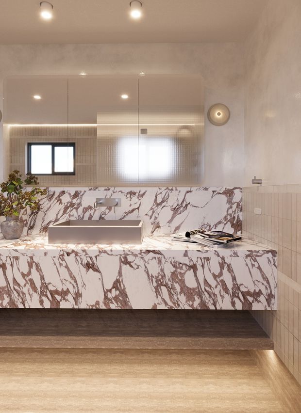 A refined contemporary bathroom featuring a large floating vanity clad in dramatic white marble with burgundy veining, an integrated rectangular basin, wall-mounted tapware, and a broad mirrored cabinet above. Warm concealed LED lighting, beige textured wall finishes, tiled side walls, and dark wood-toned flooring create a luxurious, softly illuminated interior.