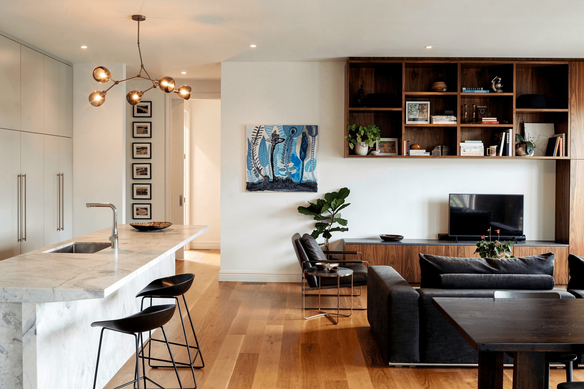 The open-plan living pavilion brings together the kitchen, dining and lounge beneath a calm material palette. Grey cabinetry, a Super White granite island with a distinctive T-shaped detail and bespoke walnut joinery create a space designed for family life and entertaining.