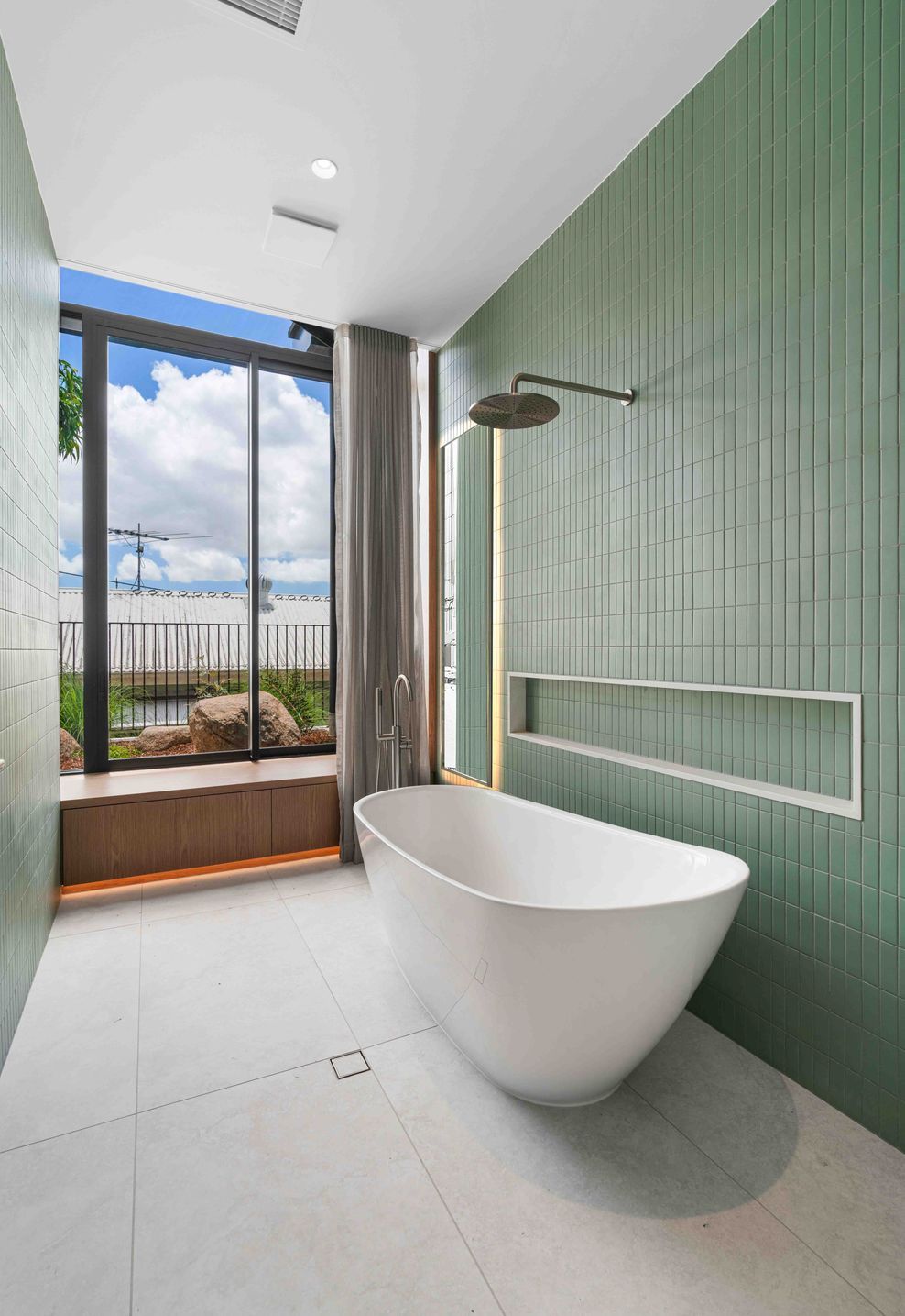 Sage green tiling and a freestanding bath give the bathroom a calm, garden-facing outlook.