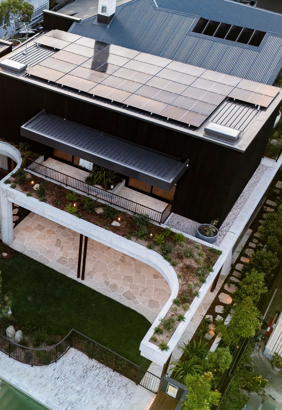Seen from above, the home's dark timber form settles into terraced gardens, with rooftop solar hidden in plain sight.