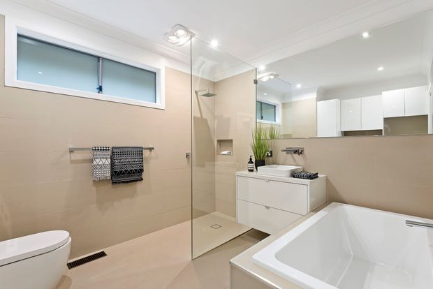 Bright contemporary bathroom featuring a frameless glass walk-in shower, freestanding-style bathtub, wall-hung white vanity, large mirrored cabinetry, beige wall and floor tiles, and white ceilings with recessed lighting. A frosted horizontal window provides natural light.