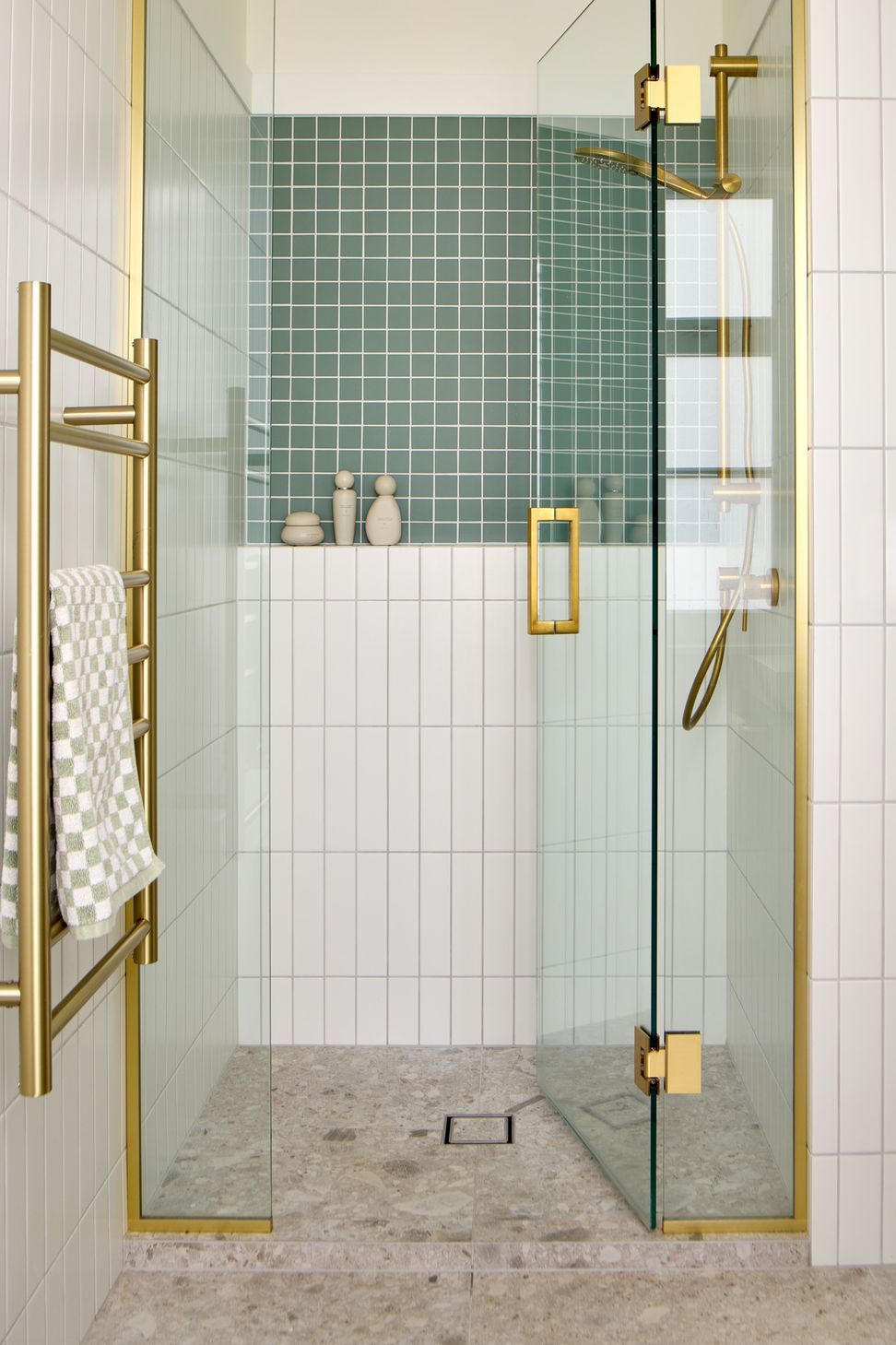 The ensuite combines timeless materials with contemporary detailing. Sandy terrazzo floor tiles are paired with white vertical subway tiles, green mosaic accents and brushed brass fittings to create a warm, inviting bathroom.