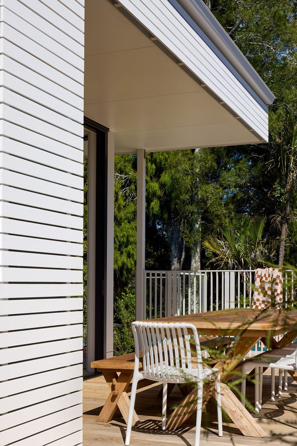 The rear deck extends directly from the living spaces to create an inviting outdoor entertaining area. A generous dining table overlooks the swimming pool, while the contemporary extension is defined by crisp white horizontal timber battens.