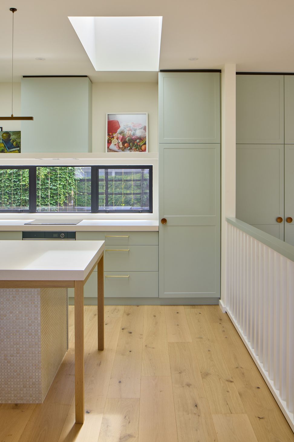 The bespoke cabinetry continues seamlessly from the kitchen into the living room, creating a unified interior. Oak flooring, white ceilings and carefully aligned skylights flood the open-plan space with natural light.