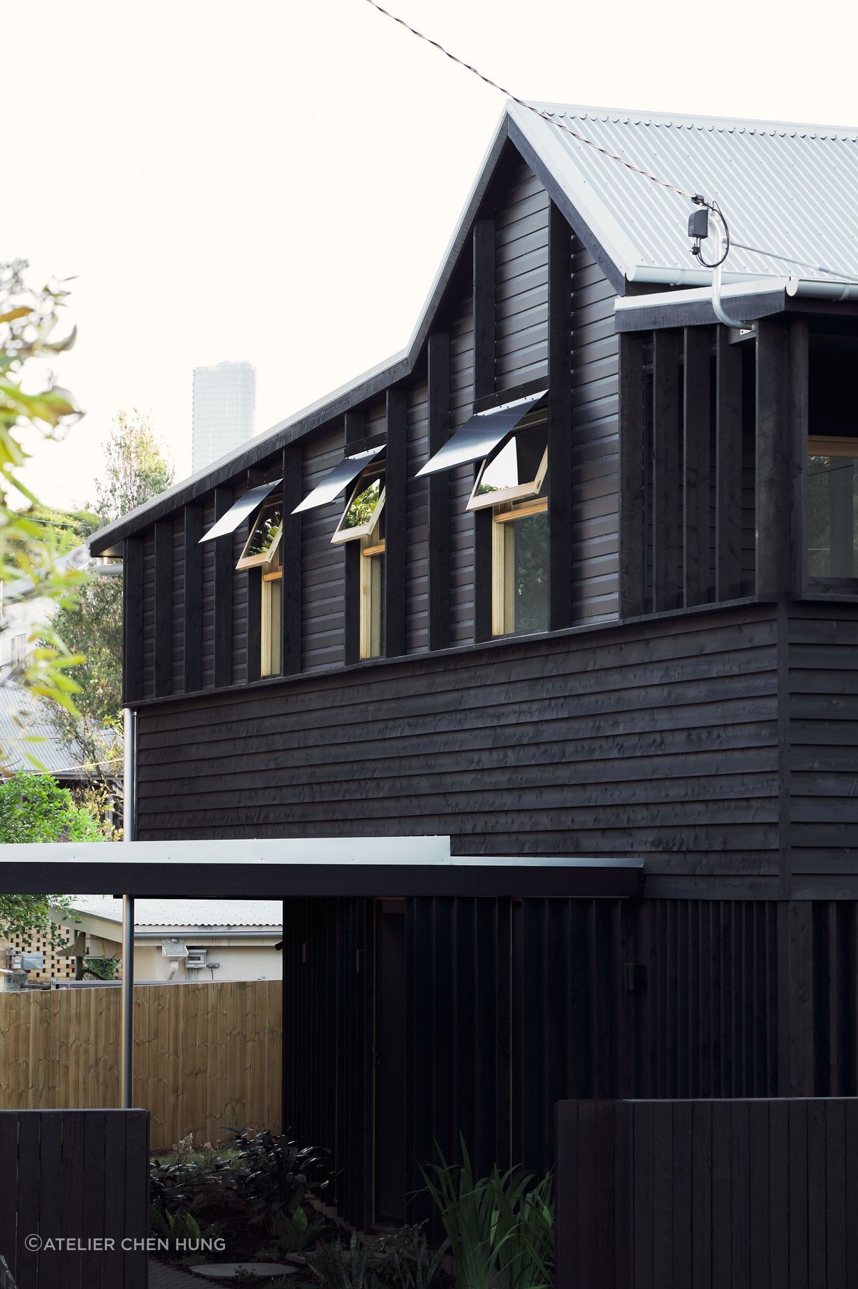 Highgate Hill Cottage’s side facade is articulated with timber studs on the existing upper band, a central horizontal band of textural weatherboard, and a lower band of vertical stud framing, unified with a transparent black stain.