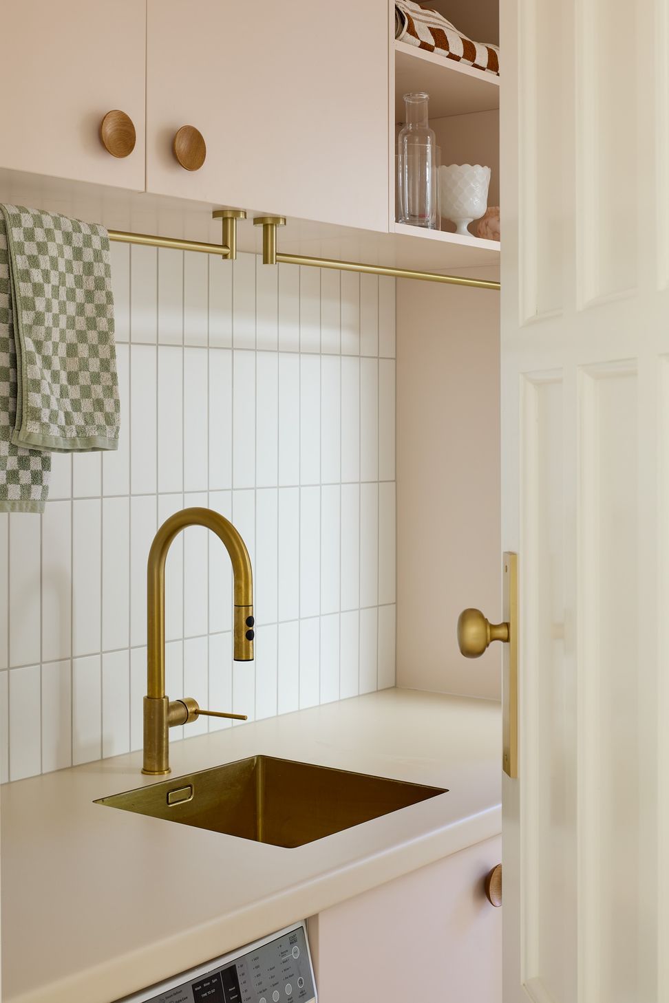 The laundry elevates an everyday space through playful colour and thoughtful detailing. Soft pink cabinetry, warm neutral benchtops, brass fixtures and white tiled splashbacks create a highly functional yet beautifully crafted utility room.
