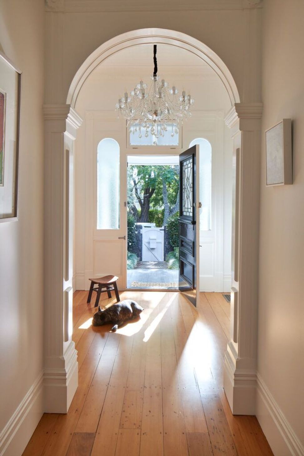 The restored hallway celebrates the villa's heritage character through polished timber floors, original detailing and a chandelier. Framed views to the front garden reinforce the home's connection to its historic setting.