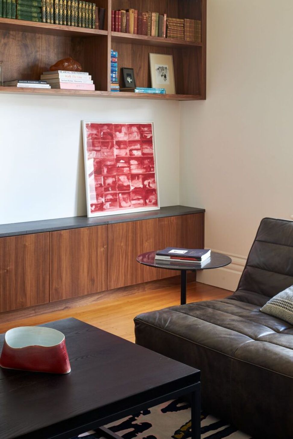 Custom walnut cabinetry with black granite tops anchors the living room, providing generous storage while complementing the warm timber flooring and vintage leather sofa.