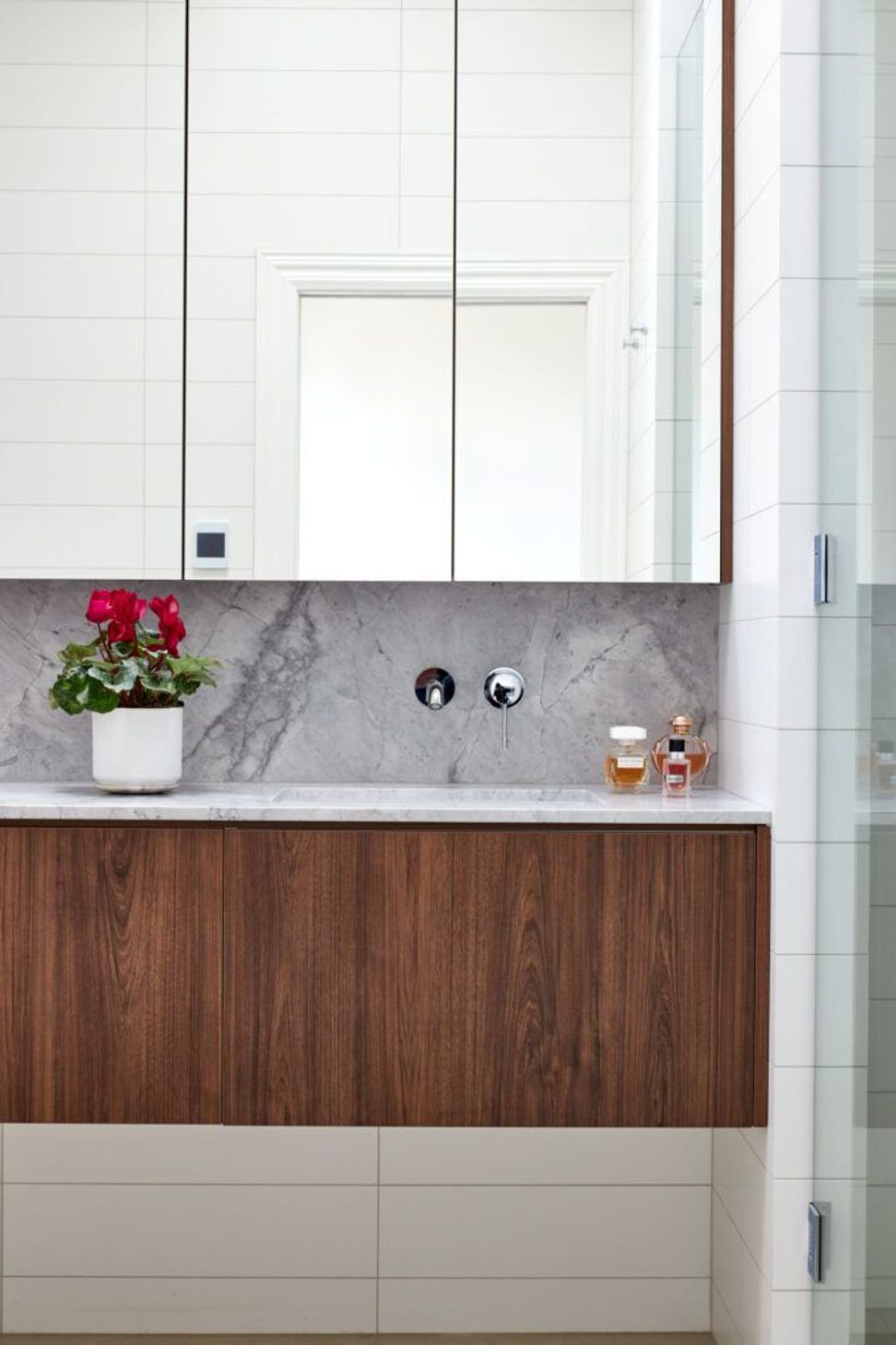 The ensuite combines walnut cabinetry, a built-in mirror cabinet and a Super White granite splashback with a restrained palette of tiled walls and floors, creating a calm and elegant retreat.