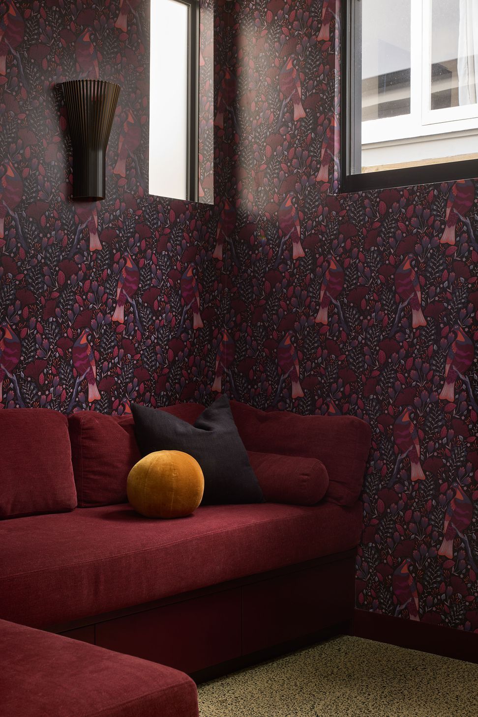 The snug offers an intimate retreat, featuring built-in seating upholstered in rich maroon velvet. Patterned wallpaper and a sculptural wall light add warmth, colour and personality to the space.