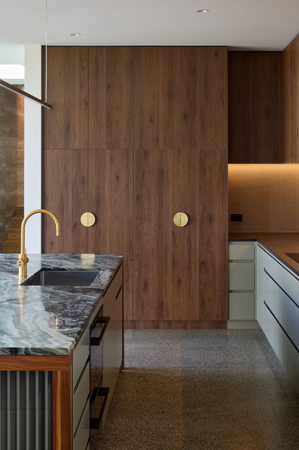 The kitchen combines walnut cabinetry with green cabinet fronts and richly veined granite benchtops. A tiled island base and carefully detailed joinery create a timeless focal point for family life.