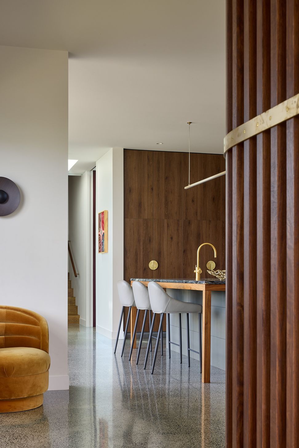 The polished concrete floor flows throughout the living spaces, while a finely crafted walnut screen introduces rhythm and texture. Beyond, the kitchen forms the social heart of the home.
